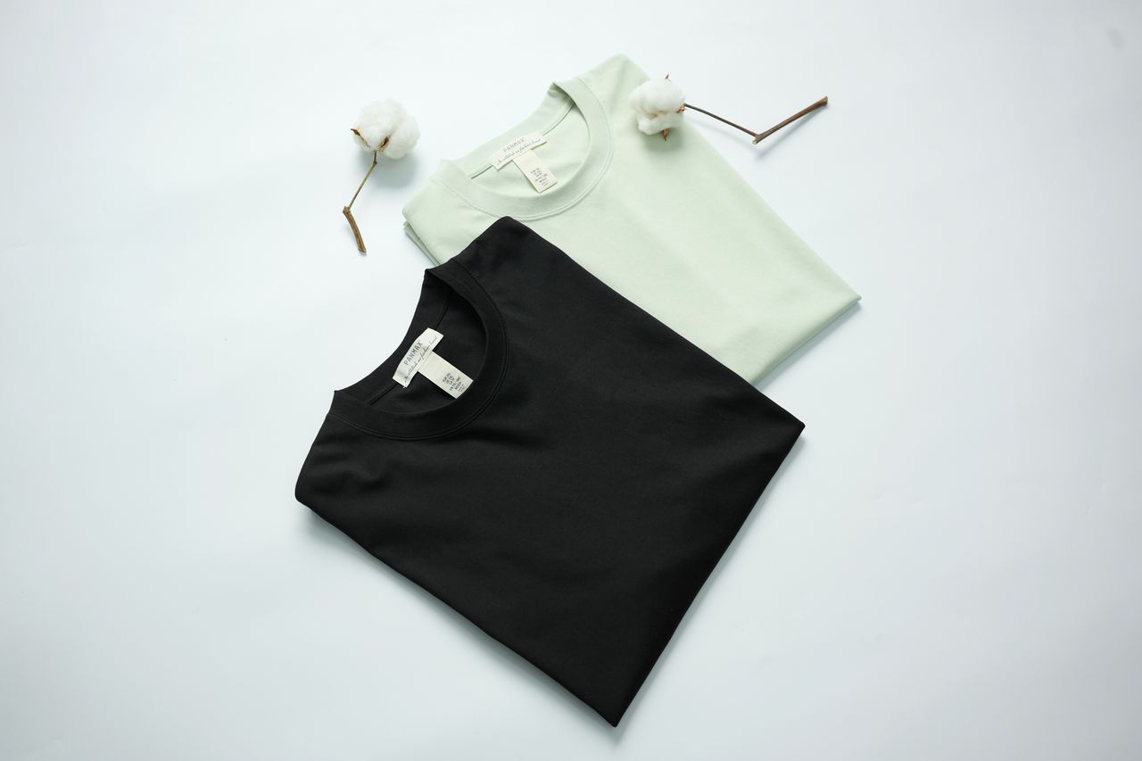Two cotton t-shirts in black and mint green on a light background with cotton flowers.